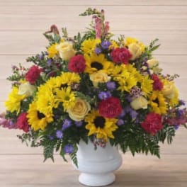 Mixed bouquet of yellow sunflowers, roses, and pink carnations in a white vase