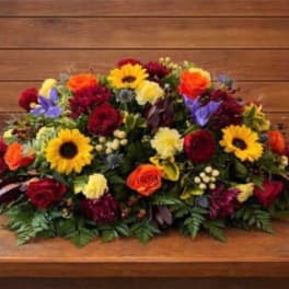 Low floral arrangement with sunflowers, roses, and mixed blooms on a wooden surface