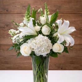 White floral arrangement in a clear glass vase with roses and lilies