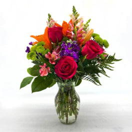 Mixed bouquet of roses, lilies, and purple flowers in a glass vase
