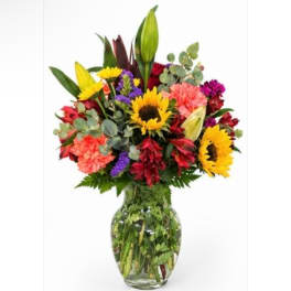 Mixed bouquet of sunflowers, lilies, and carnations in a glass vase