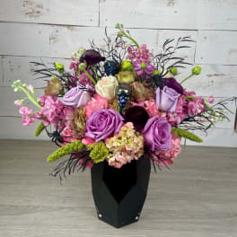 Pink and lavender rose arrangement in a black vase with skull accents