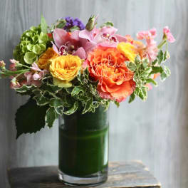 Mixed bouquet in a green glass vase with pink, orange, and yellow blooms