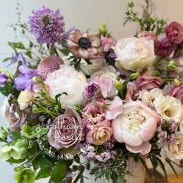 Pastel bouquet of peonies, roses, and purple blooms in a white vase