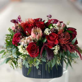 Red roses and mixed blooms arranged in a dark rectangular vase