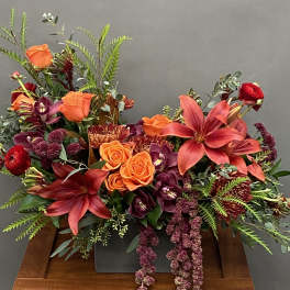 Orange and red floral arrangement with lilies and roses in a low container
