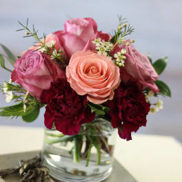 Pink and peach roses with burgundy carnations in a glass vase
