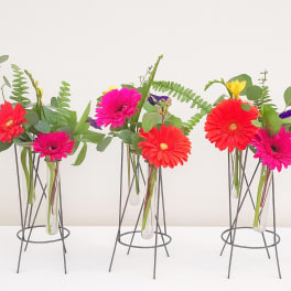 Bright gerbera daisies in slim glass vases on metal stands