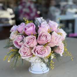 Pink roses arranged in a white pedestal vase with yellow filler flowers
