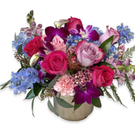 Mixed bouquet of pink roses, purple orchids, and blue flowers in a gold vase