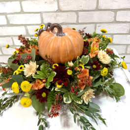 Pumpkin centerpiece surrounded by mixed fall flowers in warm colors