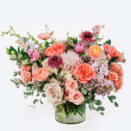 Mixed pink and peach flowers arranged in a clear glass vase
