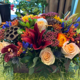 Mixed bouquet with cream roses, orchids, and bright tropical blooms in a wooden box