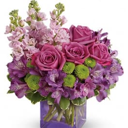 Purple roses and mixed purple flowers in a square glass vase