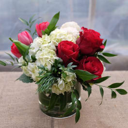 Red roses and pink tulips arranged with white hydrangeas in a glass vase.