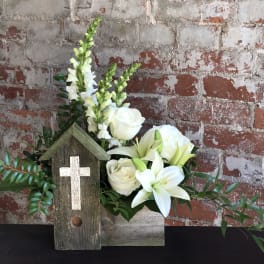 White flowers arranged in a rustic wooden box with a small cross plaque