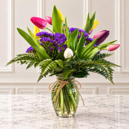 Colorful tulips and purple filler flowers in a glass vase with a twine bow