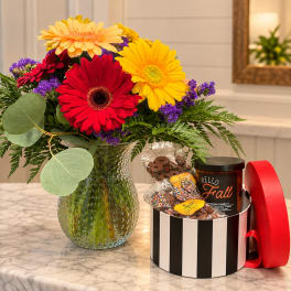 Colorful gerbera bouquet in a textured glass vase beside a candy gift box