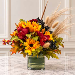 Autumn bouquet with yellow sunflowers, red blooms, and dried grasses in a glass vase