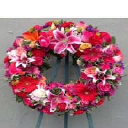 Circular floral wreath with pink, red, and white blooms on a stand