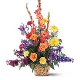Tall mixed arrangement of orange, yellow, and purple flowers in a woven basket