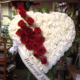 Heart-shaped white floral wreath with red roses and a ribbon