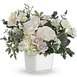 White floral arrangement in a square white vase with greenery