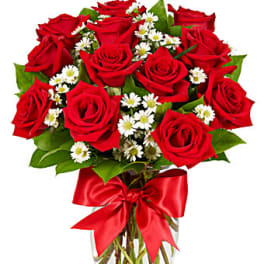 Arrangement of red roses and small white daisies in a clear glass vase with a red satin bow