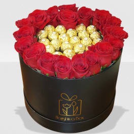 Round black hat box filled with red roses surrounding gold-wrapped chocolates