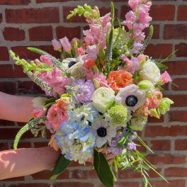 Handheld bouquet of pastel pink, white, blue, and peach flowers