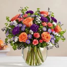 Bouquet of orange roses, purple flowers, and pink carnations in a glass vase