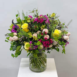 Mixed bouquet of yellow, pink, and purple flowers in a glass vase