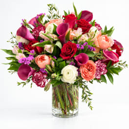 Mixed bouquet of roses, calla lilies, and ranunculus in a clear glass vase