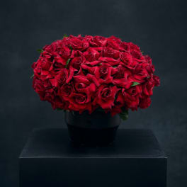 Red rose bouquet in a black vase on a dark pedestal