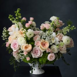 Pastel rose and ranunculus arrangement in a white pedestal vase
