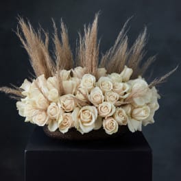Cream rose arrangement with tall dried grass accents in a dark bowl