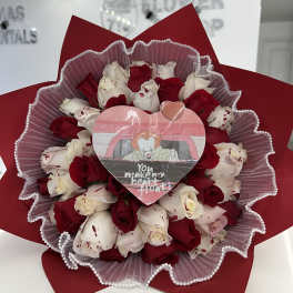 Red and white rose bouquet wrapped in red paper with a heart topper