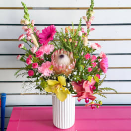 Bright mixed bouquet in a white ribbed vase with pink, yellow, and orchid blooms