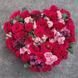 Heart-shaped bouquet of pink and red roses with small purple accents