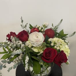 Red and white roses with hydrangeas in a glass vase, accented with ornaments
