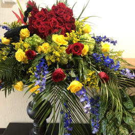 Large standing arrangement of red and yellow roses with blue flowers in a black vase