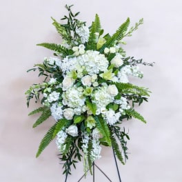 Large white floral standing spray with roses and lilies on a black easel