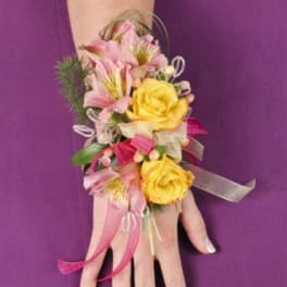 Pink and yellow floral wrist corsage on a hand