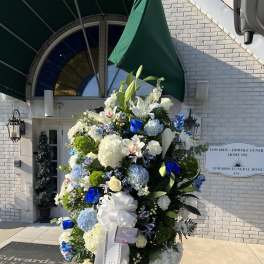 Large funeral spray of white, blue, and green flowers on an easel