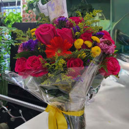 Bouquet of hot pink roses and mixed flowers wrapped in clear plastic with a yellow ribbon