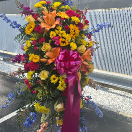Large standing floral spray with yellow, pink, orange, and blue flowers and a magenta bow