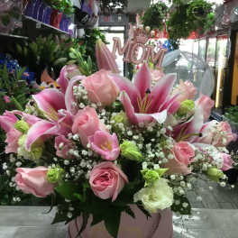 Pink lilies and roses arranged in a round pink box.