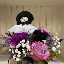 Purple and pink floral arrangement in a black spiderweb vase with a small skeleton figure