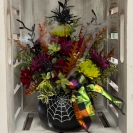 Halloween floral arrangement in a black spiderweb vase with colorful blooms and ribbon