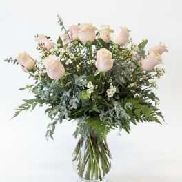 Blush pink roses in a clear glass vase with mixed greenery